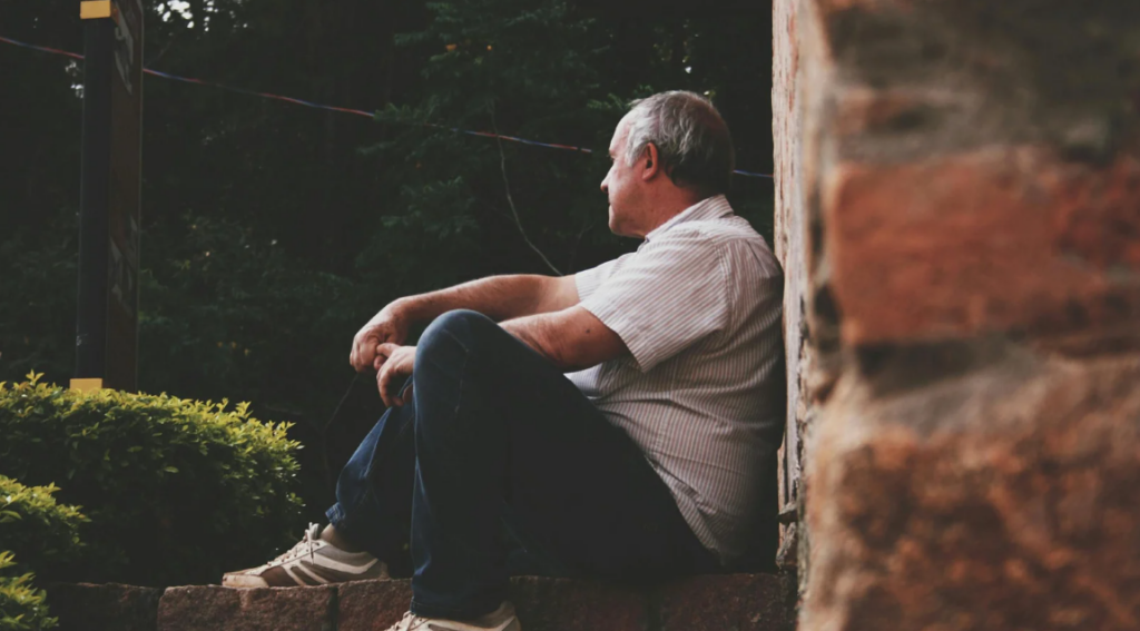 senior sitting on a stair while leaning on a brick wall